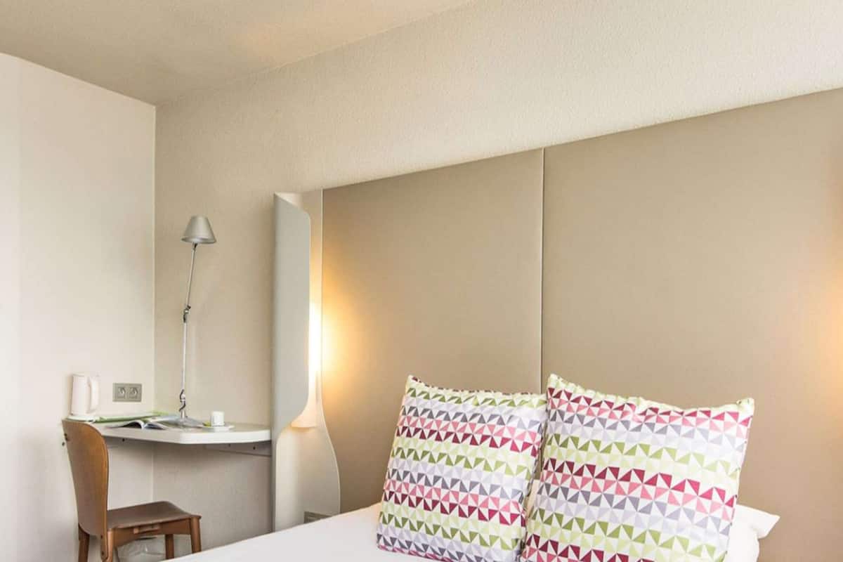 A hotel room with a bed, a desk, a chair, and a lamp.