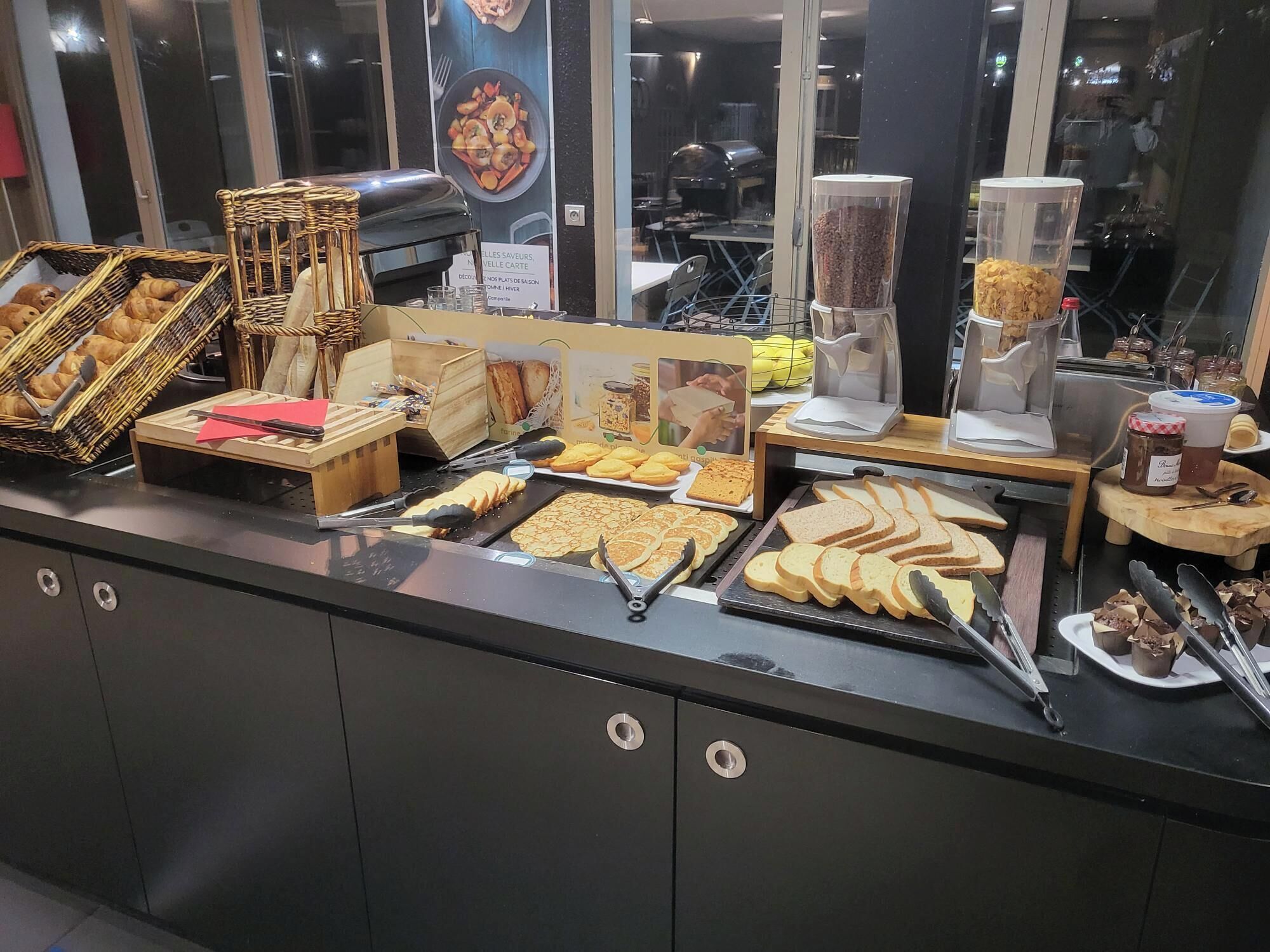 A buffet counter with various food items, including pastries, sandwiches, and sliced bread.