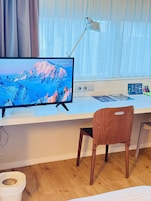 Una habitación con un escritorio, un monitor de computadora que muestra un paisaje, una lámpara y una silla.