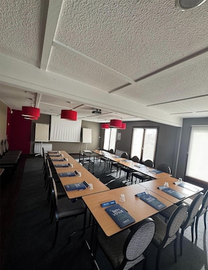 Ett konferensrum med långa bord, stolar, röda hänglampor och en projektorduk.