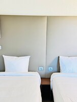Habitación de hotel con dos camas, cabecera en tonos neutros y una mesita de noche con toma de corriente.