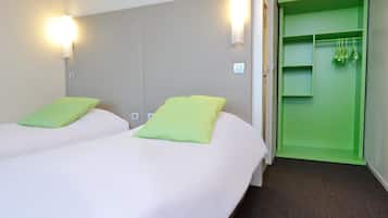 Habitación de hotel con dos camas, cada una con un almohadón verde, un armario verde y un interruptor de luz en la pared.