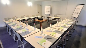 Un salón de conferencias con varias mesas, tarjetas de identificación, botellas de agua y pantallas de presentación.