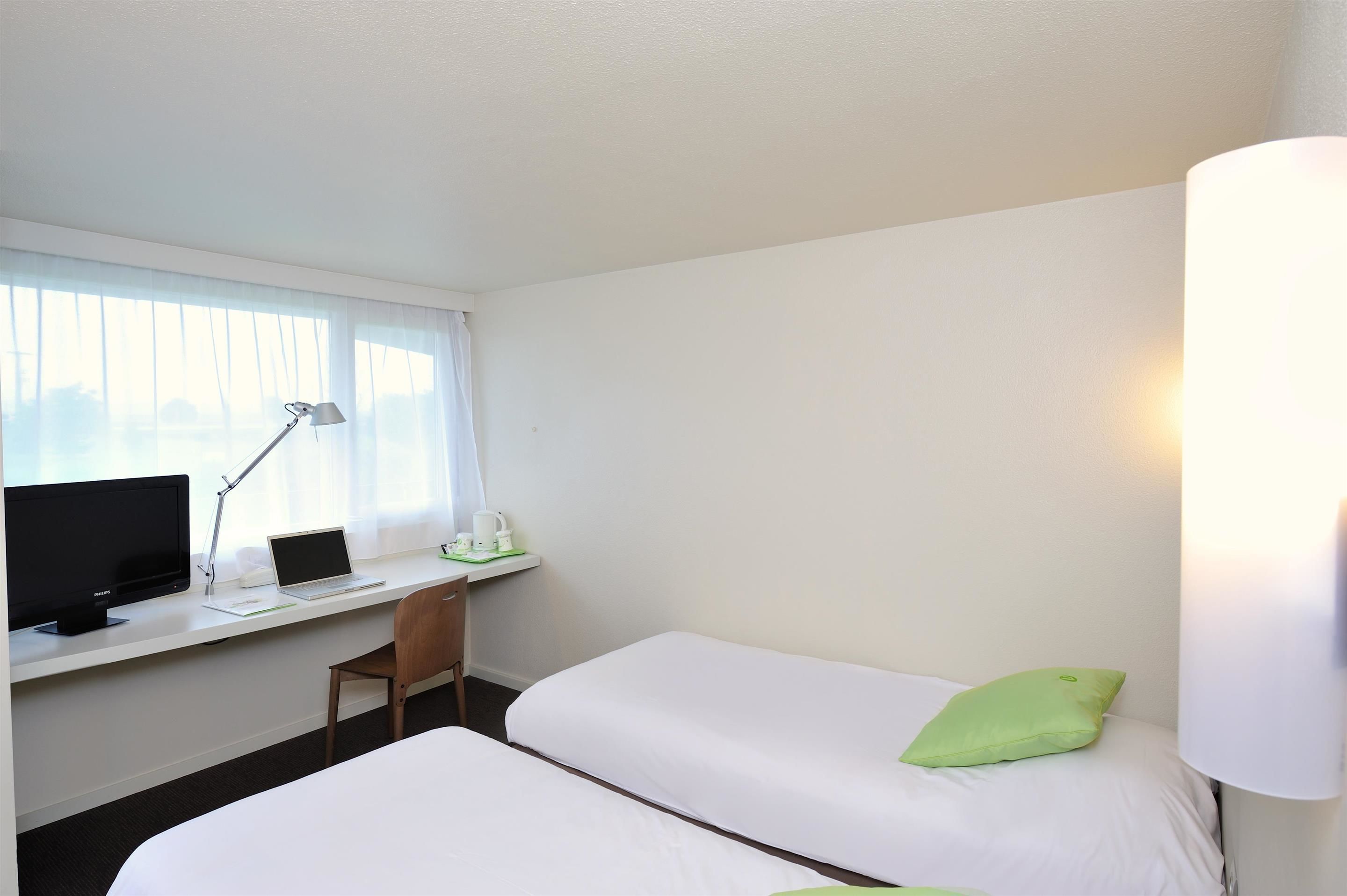 Une chambre d’hôtel équipée d’un bureau, de deux lits, d’une chaise, d’un ordinateur et d’une lampe.