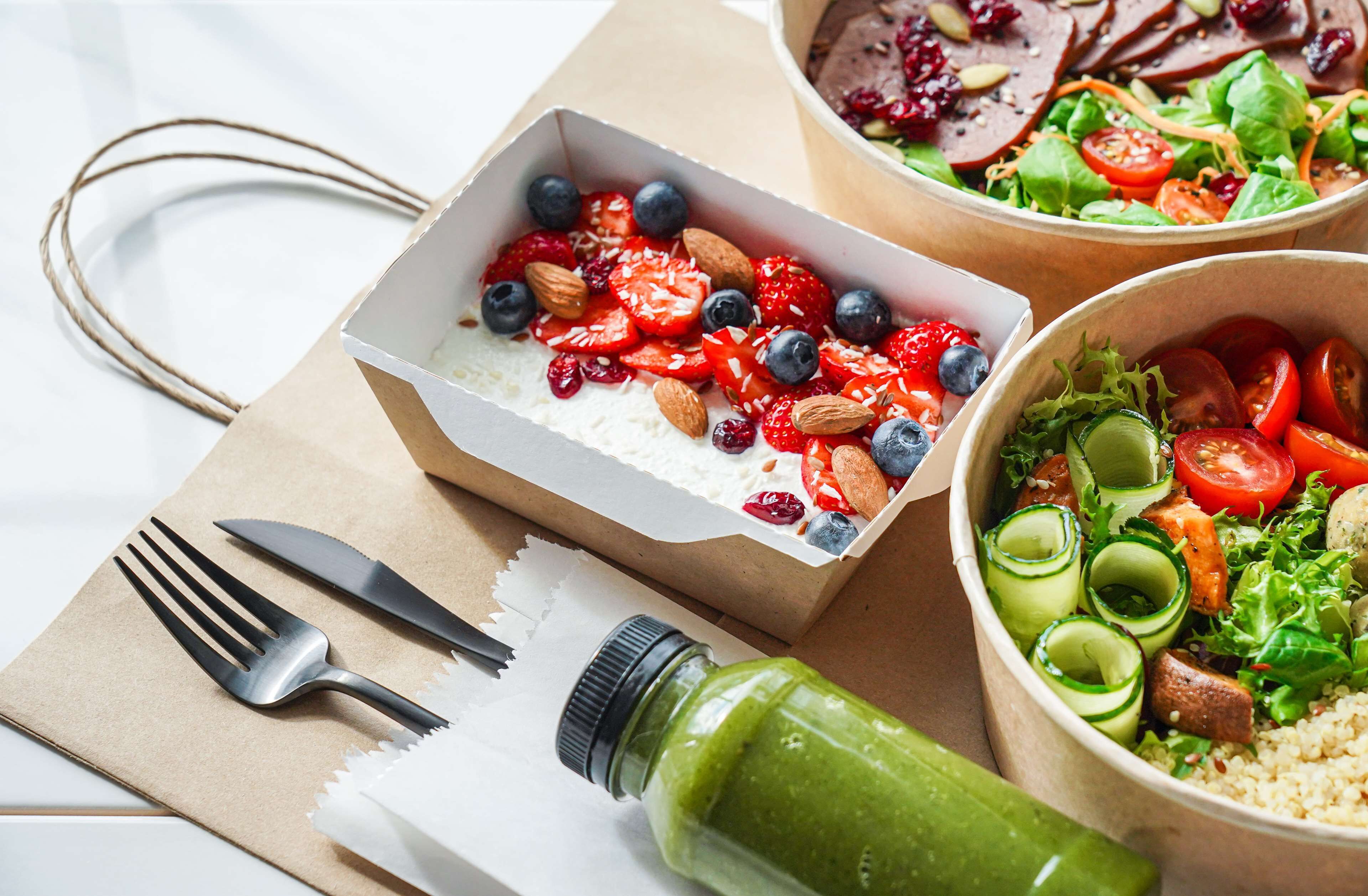 A meal setup with a bowl of salad, a bowl of yogurt with fruits, and a green smoothie bottle.