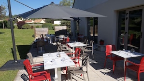 Un patio al aire libre con mesas y sillas, un paraguas grande y vistas del vecindario circundante.