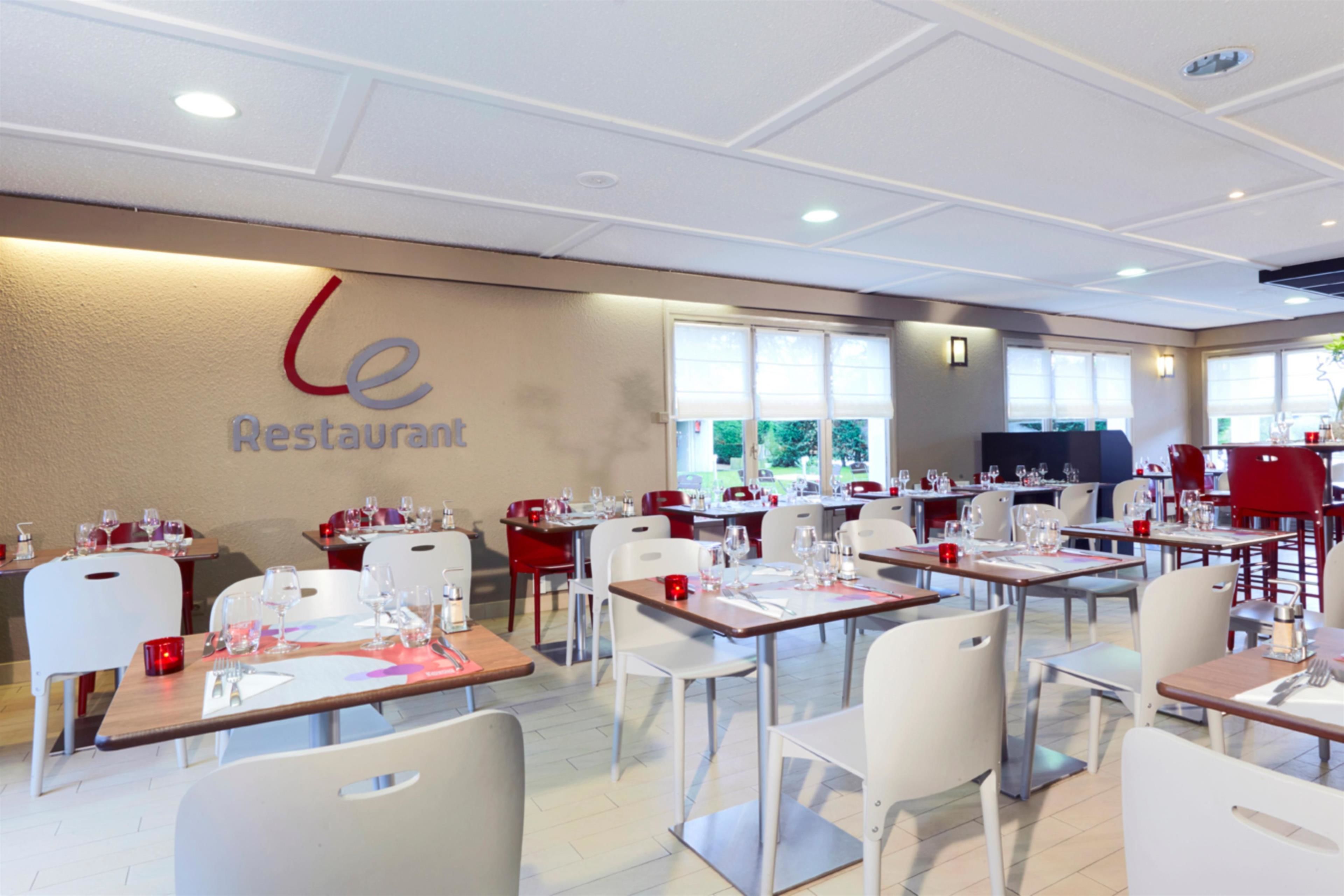 Un restaurante con mesas dispuestas para comer, sillas y una pared con el nombre del restaurante.