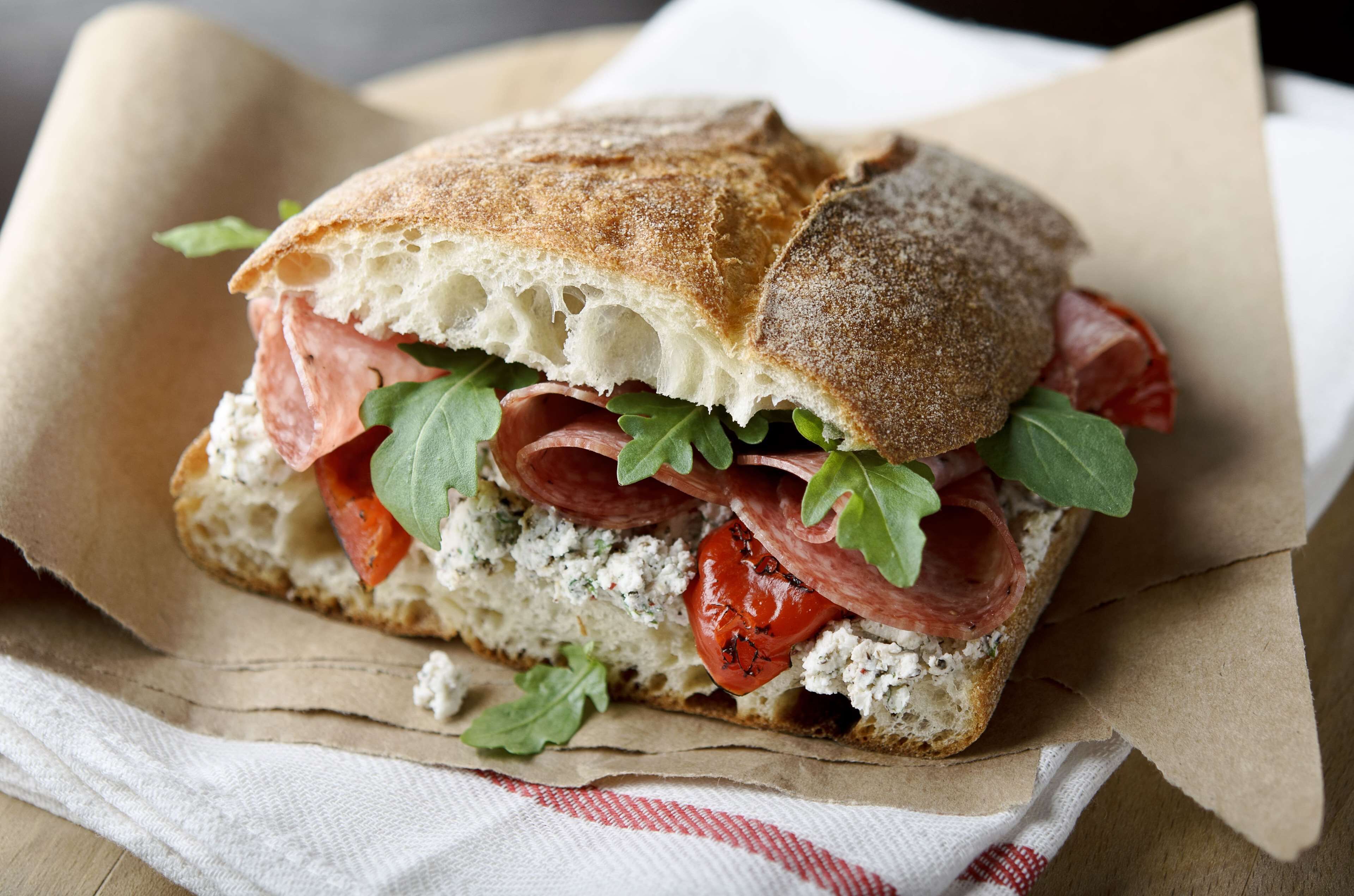 A sandwich with various ingredients on a piece of bread, placed on a paper wrapper.