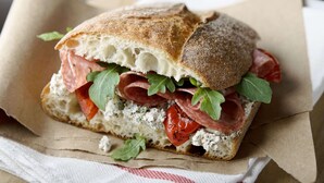 Un sándwich con varios ingredientes sobre una rebanada de pan, envuelto en papel.