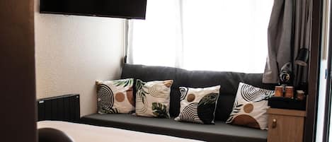 Habitación de hotel con una cama, un televisor de pantalla plana montado en la pared, una ventana con cortinas y una mesita de noche con una lámpara.