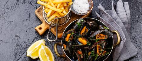 Mejillones en una olla, una cesta de papas fritas y un cuenco pequeño de sal sobre una superficie rugosa.