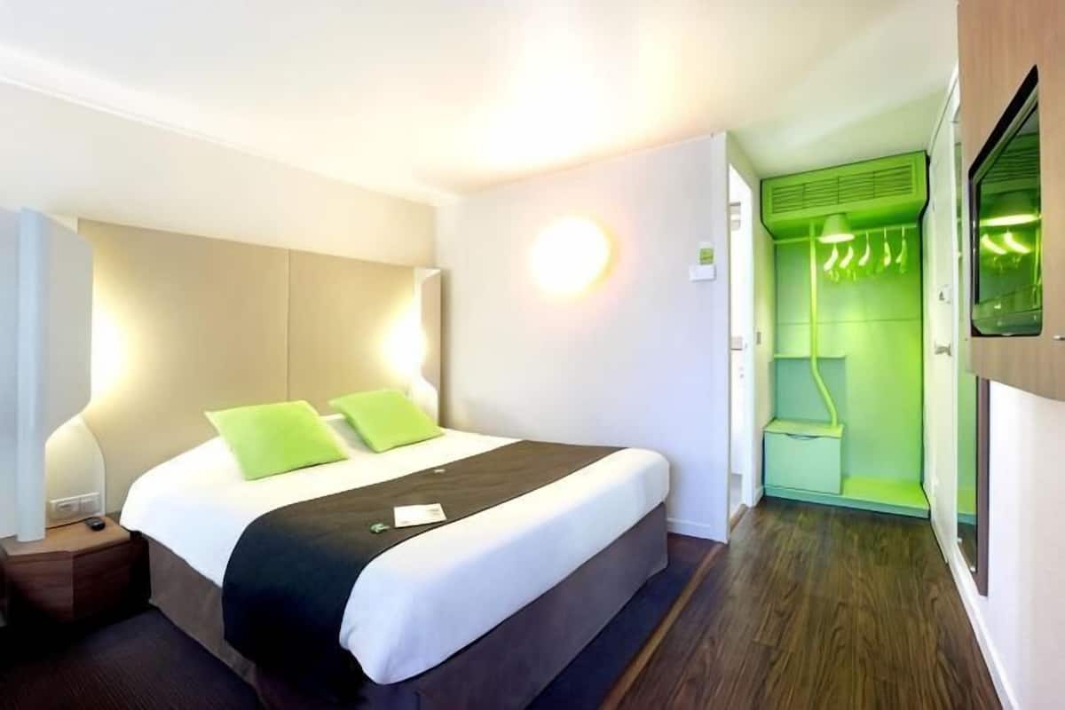 A hotel room with a bed, bedside table, and a green wall with a hanging light fixture.
