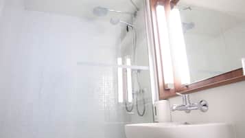 Uma casa de banho com cabine de chuveiro em vidro, uma pia branca e um espelho sobre a pia.
