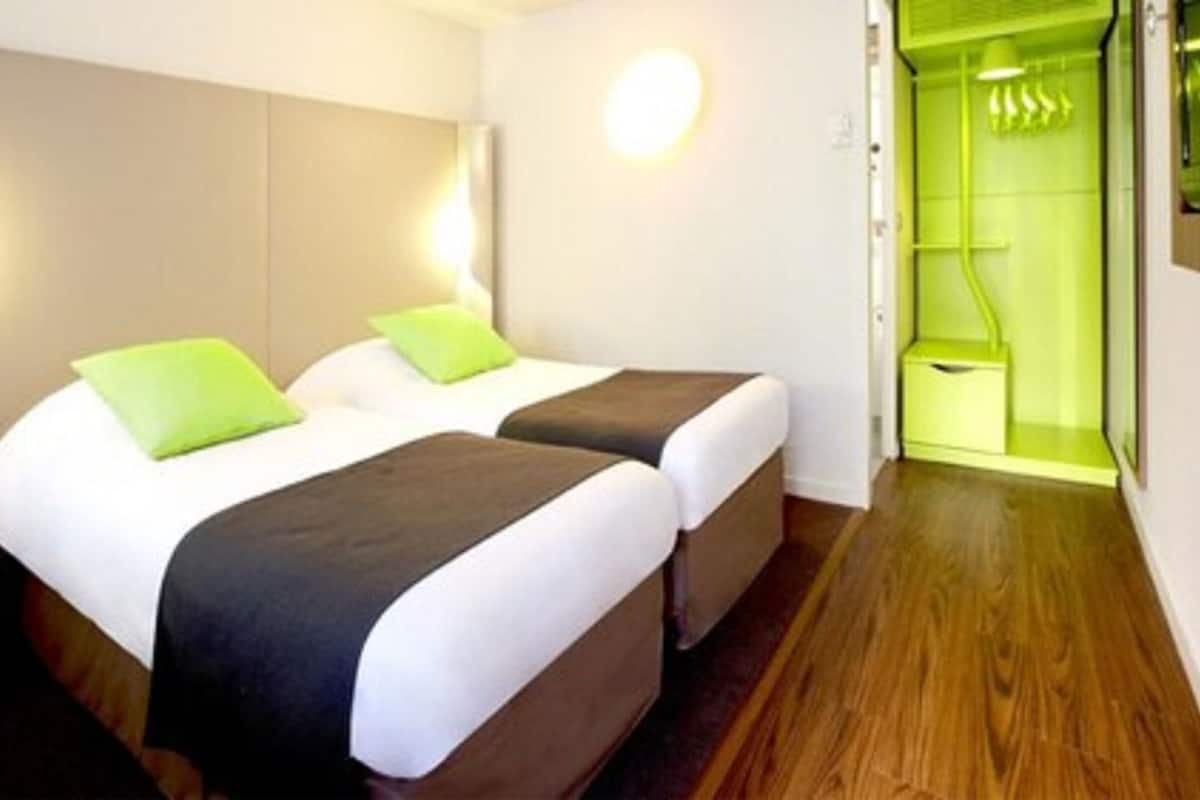 A hotel room with two beds, a wooden floor, and a green-lit shower area.