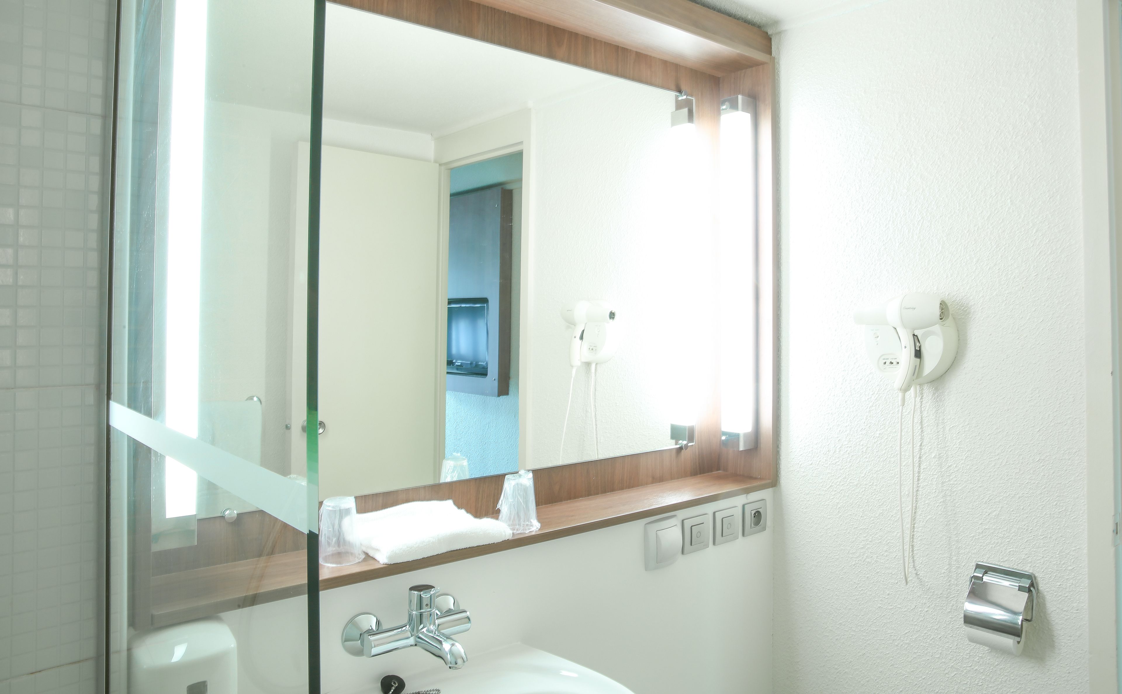 A bathroom with a glass shower enclosure, a white sink, a mirror, and a hairdryer mounted on the wall.