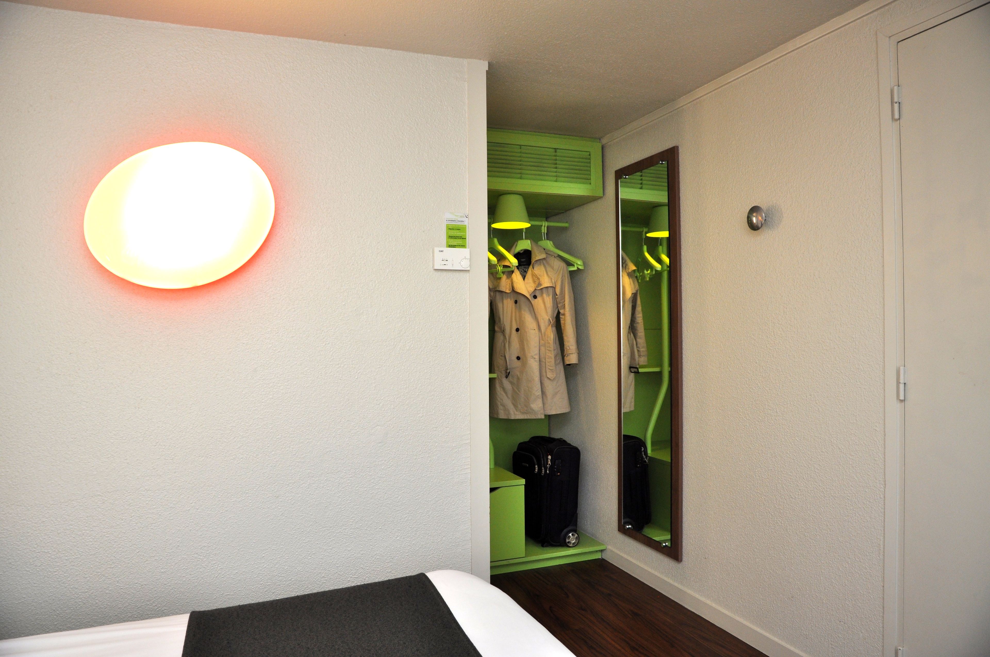 Een hotelkamer met een bed, een spiegel, een kapstok met kleding en een koffer.
