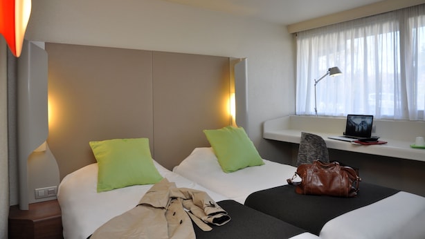 A hotel room with two beds, a desk with a laptop, a window with curtains, and a lamp. - Hôtel Inn Design & Restaurant Nantes (Sainte-Luce-sur-Loire)