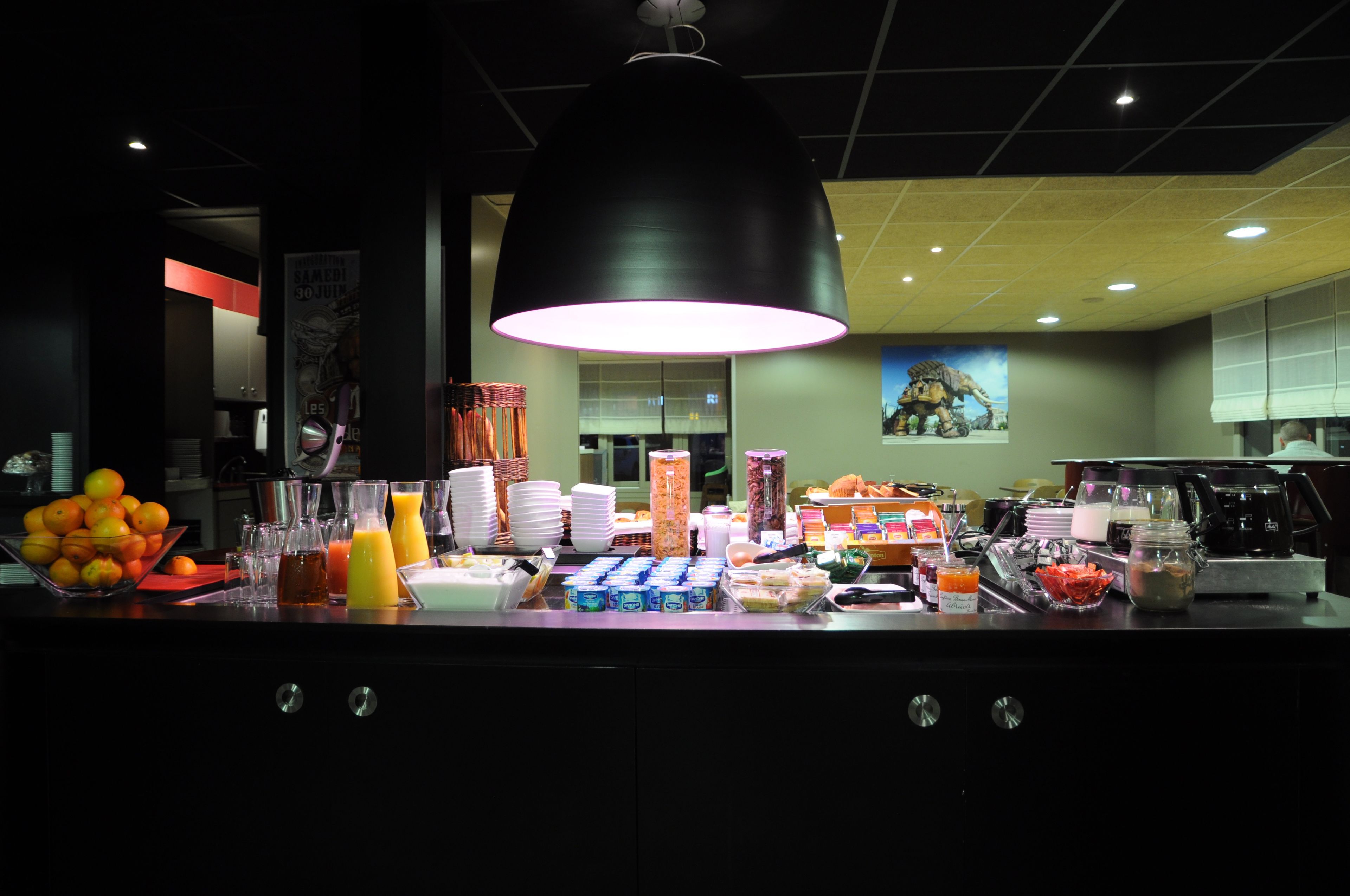 A breakfast bar with various food items and beverages, a large pendant light, and a poster on the wall.