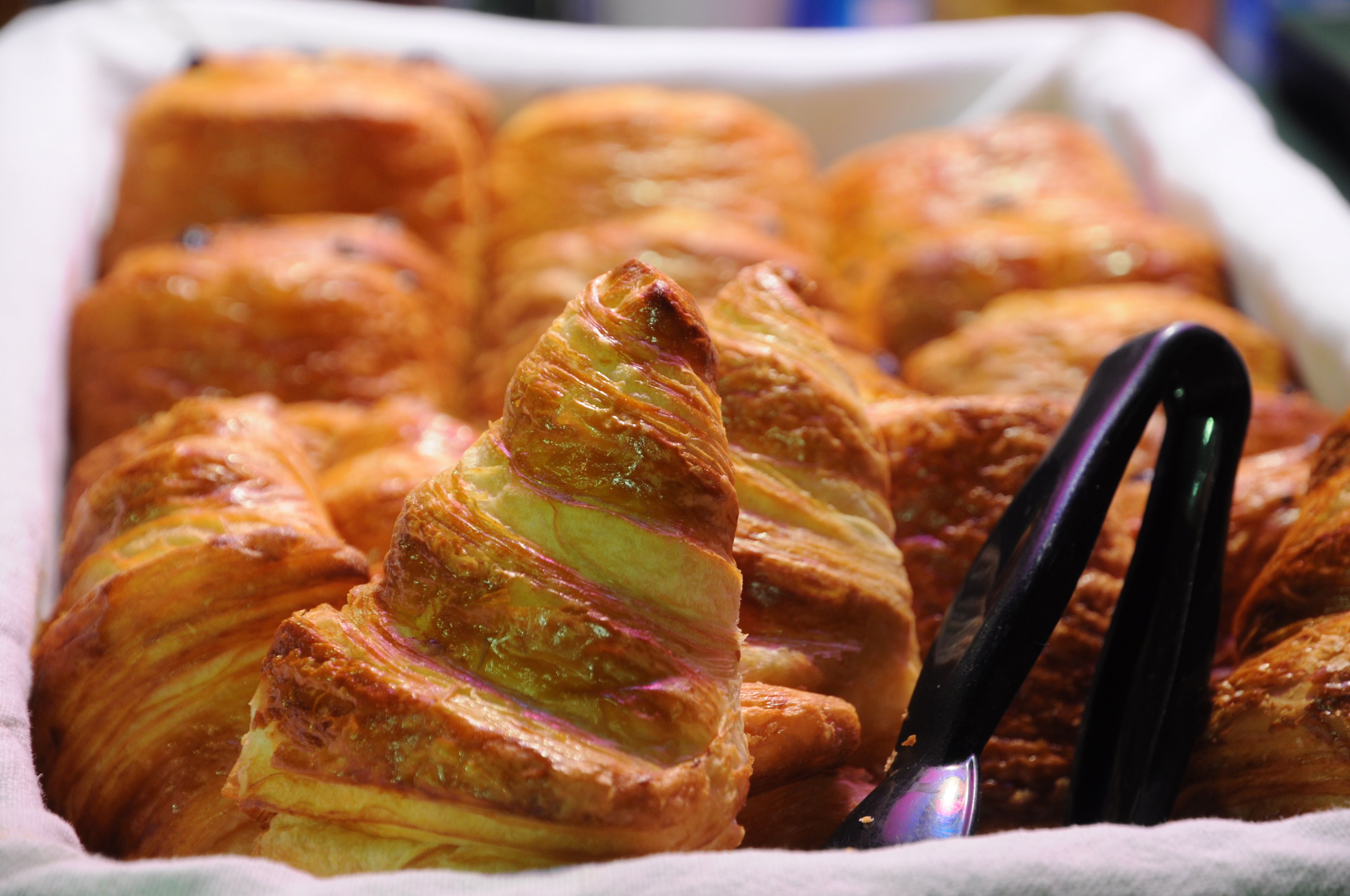 A tray of golden-brown pastries, likely croissants, with a shiny glaze and a decorative twist on one.