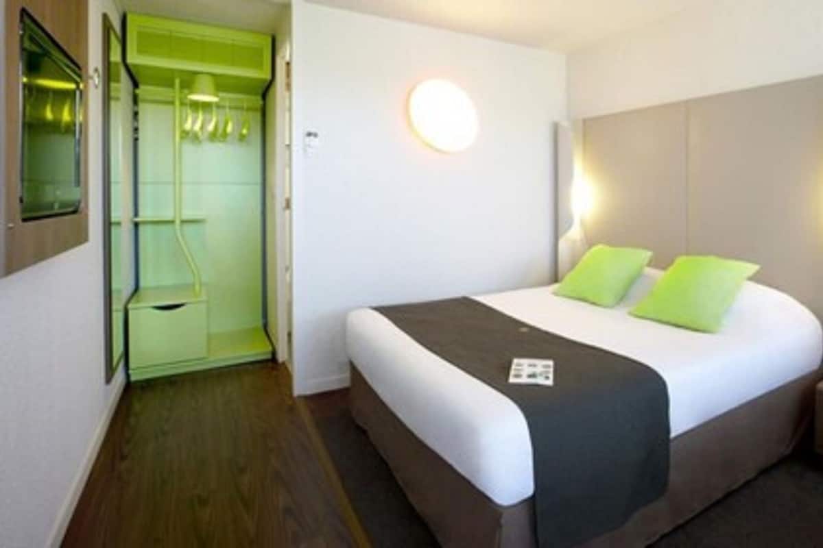 A hotel room with a bed, a nightstand, a bedside lamp, a wall-mounted light, and a green door.