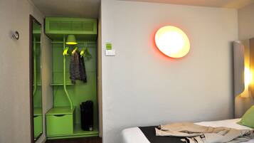 Une chambre d’hôtel avec un lit, une armoire verte, un miroir et une lampe fixée au mur.