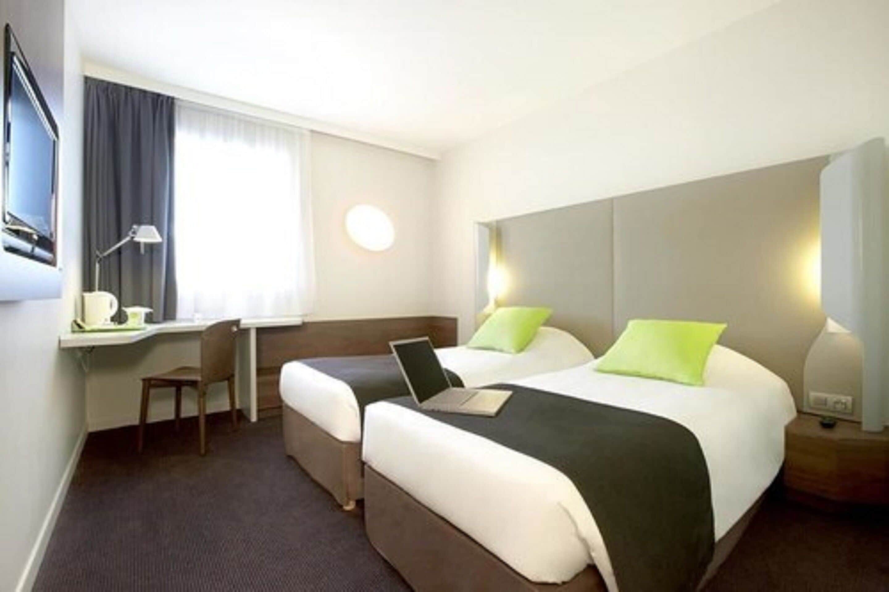 A hotel room with two beds, a desk, a chair, and a TV.