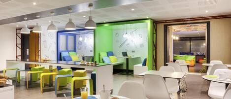 Un espace repas moderne avec un îlot central, des tables blanches et des chaises colorées.