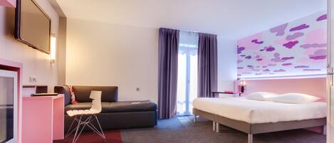 A modern hotel room with a bed, a desk, a chair, and a television.