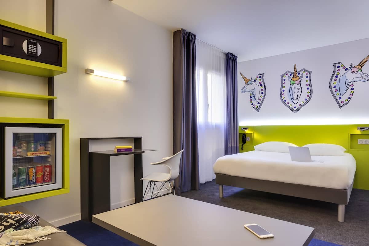 Habitación de hotel con cama, escritorio, silla, minibar y pared decorada con vinilos de unicornios.
