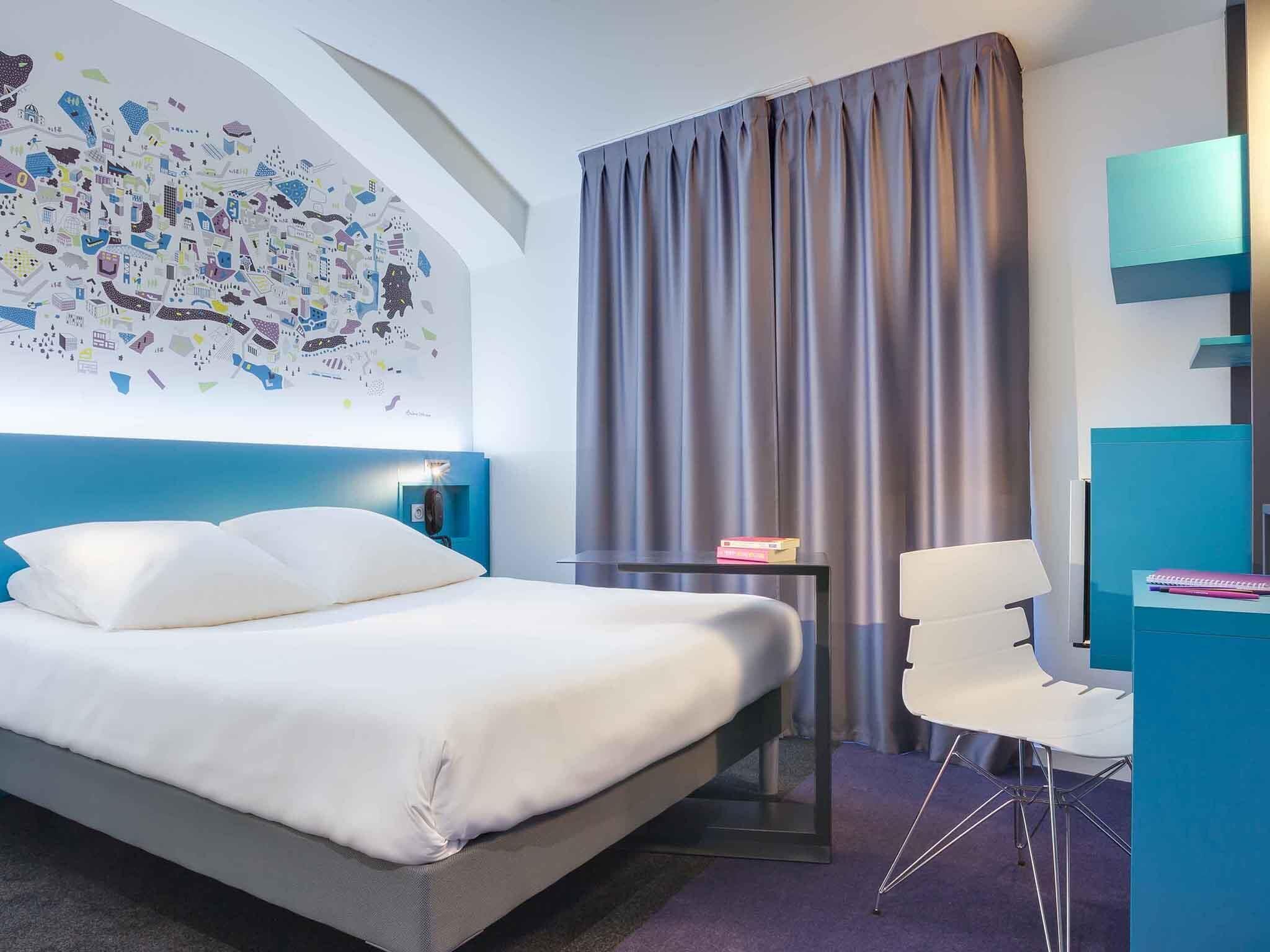 Una habitación de hotel moderna con una cama grande, un escritorio, una silla y un mural con vistas a la ciudad.