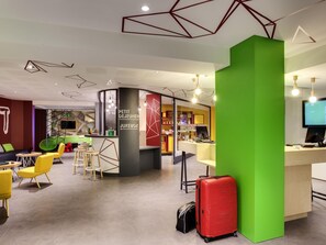 A modern hotel lobby with a bar area, seating, and a large green pillar.