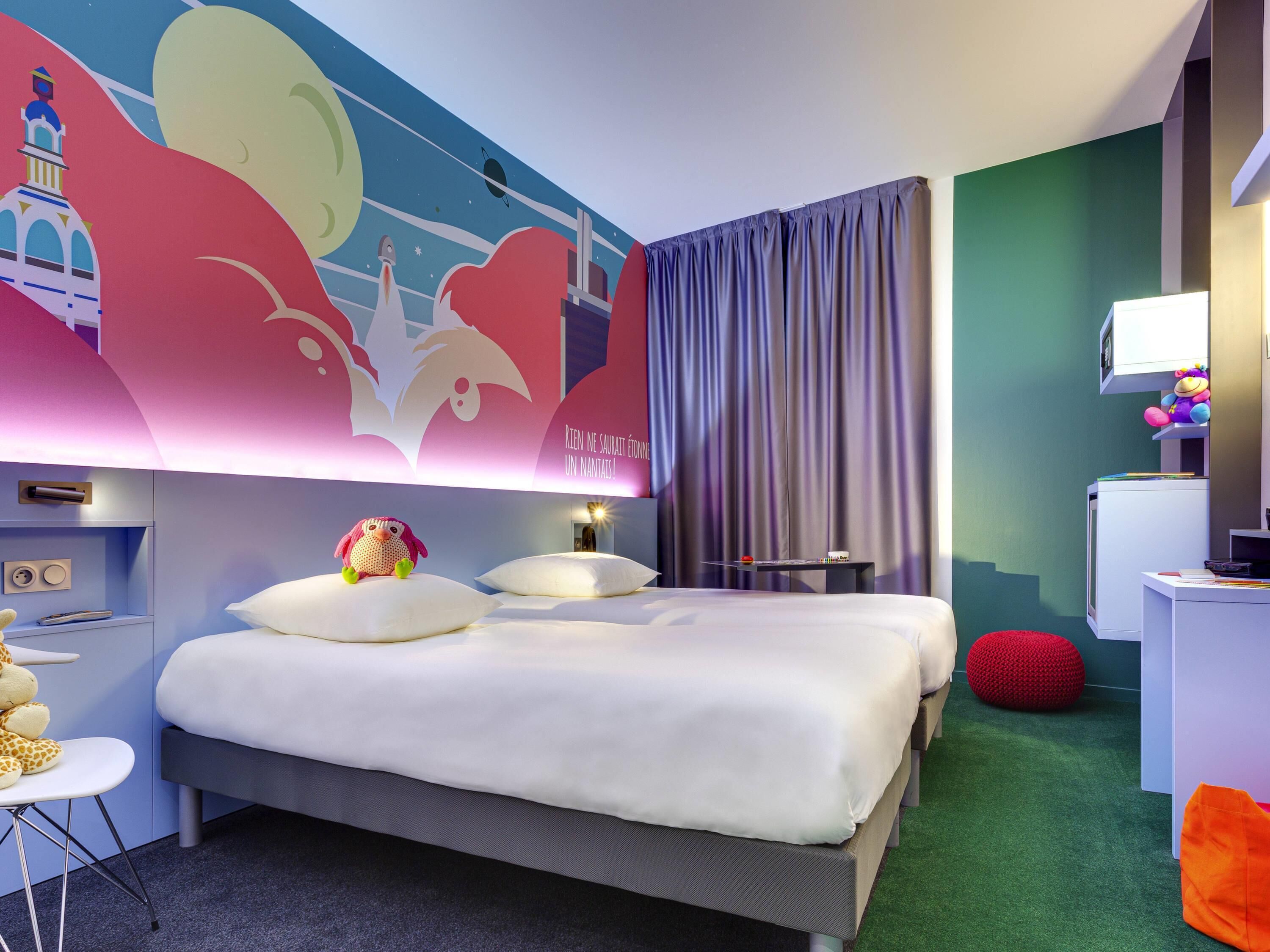 Habitación de hotel con cama, escritorio, silla, un sillón inflable rojo y un mural en la pared.
