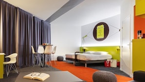 Una habitación de hotel moderna con una cama, un escritorio, una silla, un sofá y una obra de arte colgada en la pared.