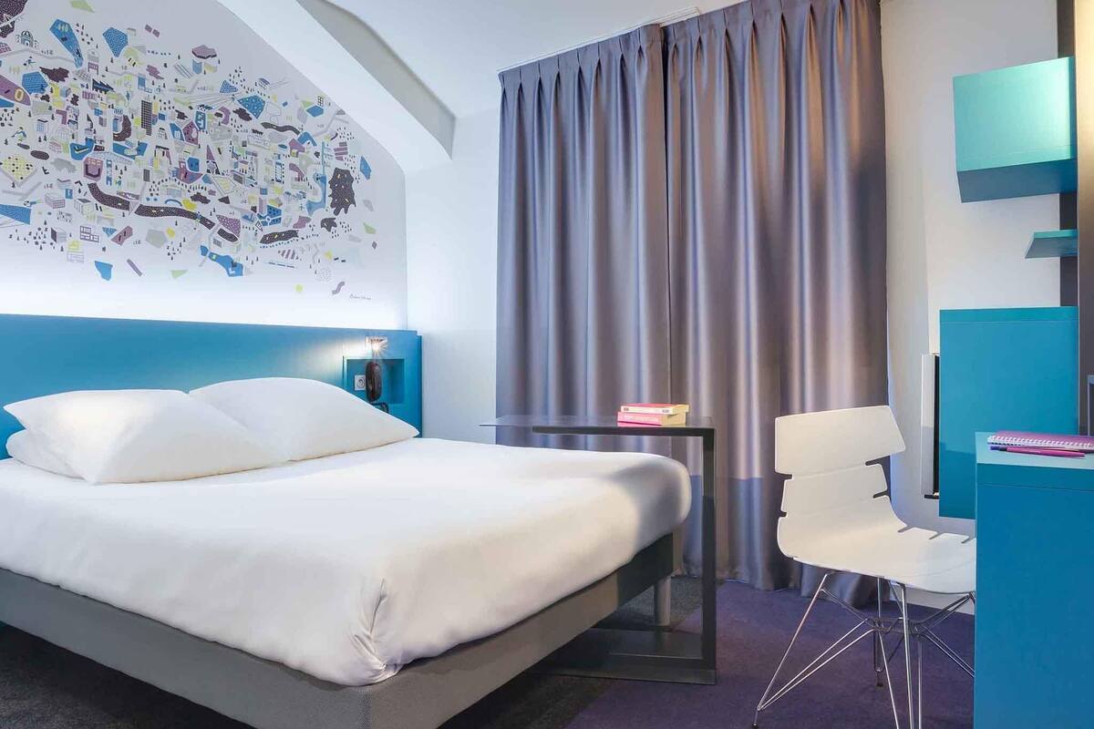 Una habitación de hotel moderna con una cama grande, un escritorio, una silla, un mural con un mapa y una cortina.