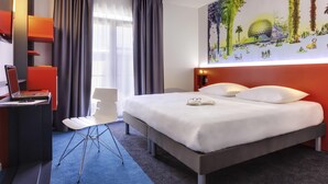 Una habitación de hotel moderna con una cama grande, un escritorio con una computadora portátil, una silla y una pared con un mural colorido.