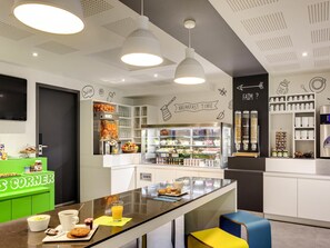 Una barra de desayuno moderna con una máquina de café, dispensador de zumo y diversas opciones para desayunar.