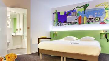Une chambre d’hôtel moderne avec un lit, un mur d’accent vert, une salle de bain avec une porte en verre et une fresque murale colorée représentant un paysage urbain.