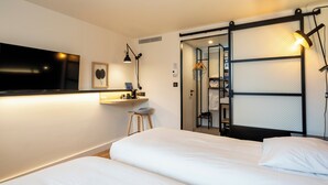 A hotel room with a large flat-screen TV, a desk with a lamp, a bed with white linens, and a sliding closet door. - Campanile NATURE - Metz Sud Jouy aux Arches (Jouy-aux-Arches)