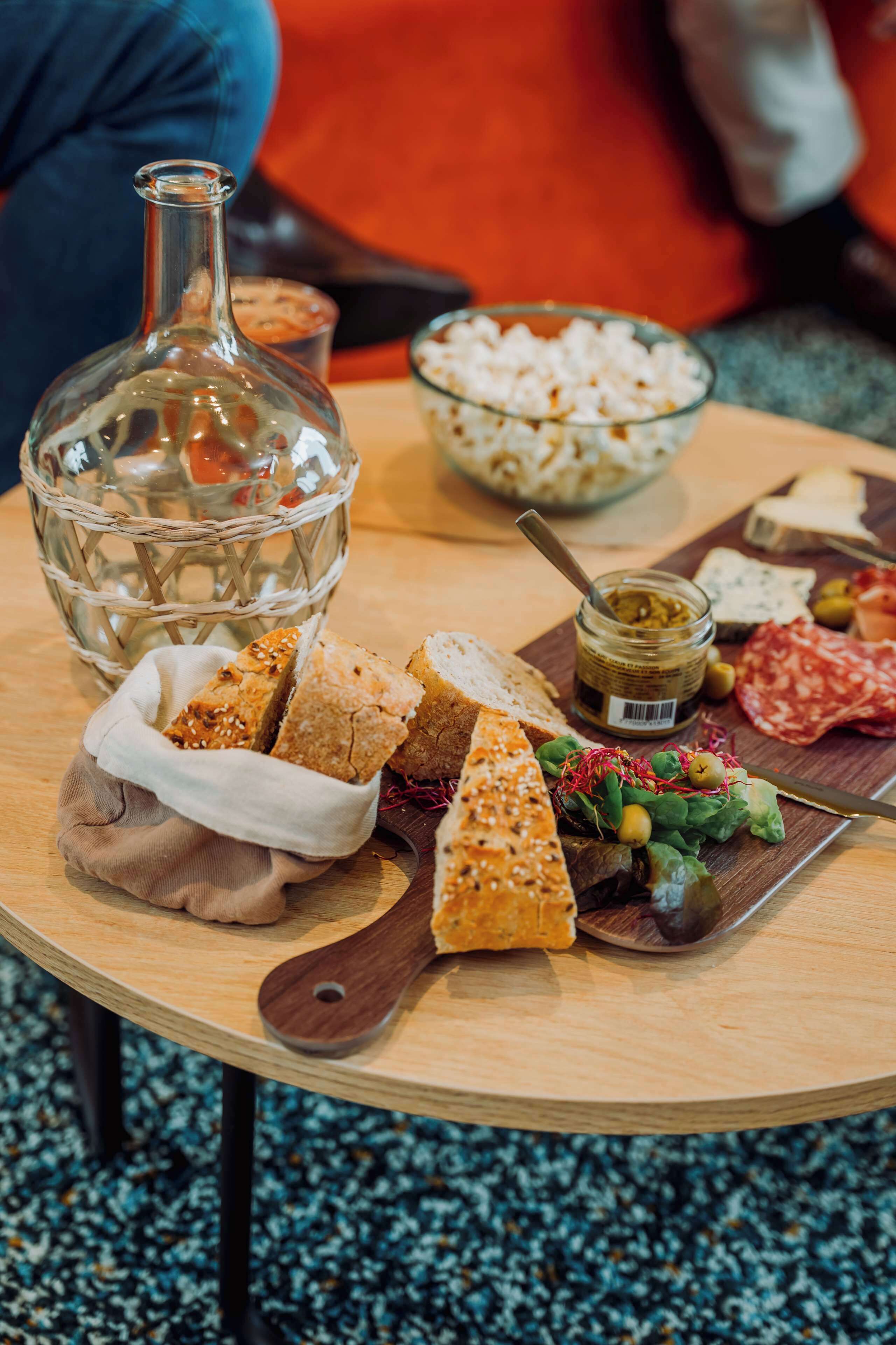 A wooden table with a variety of food items including bread, cheese, olives, and a bottle.