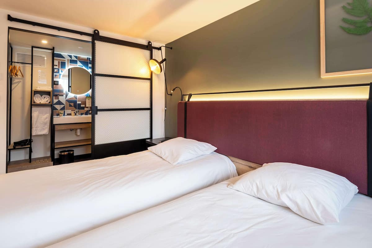 A hotel room with two beds, a large mirror, a vanity with a mirror, and a wall-mounted light fixture.