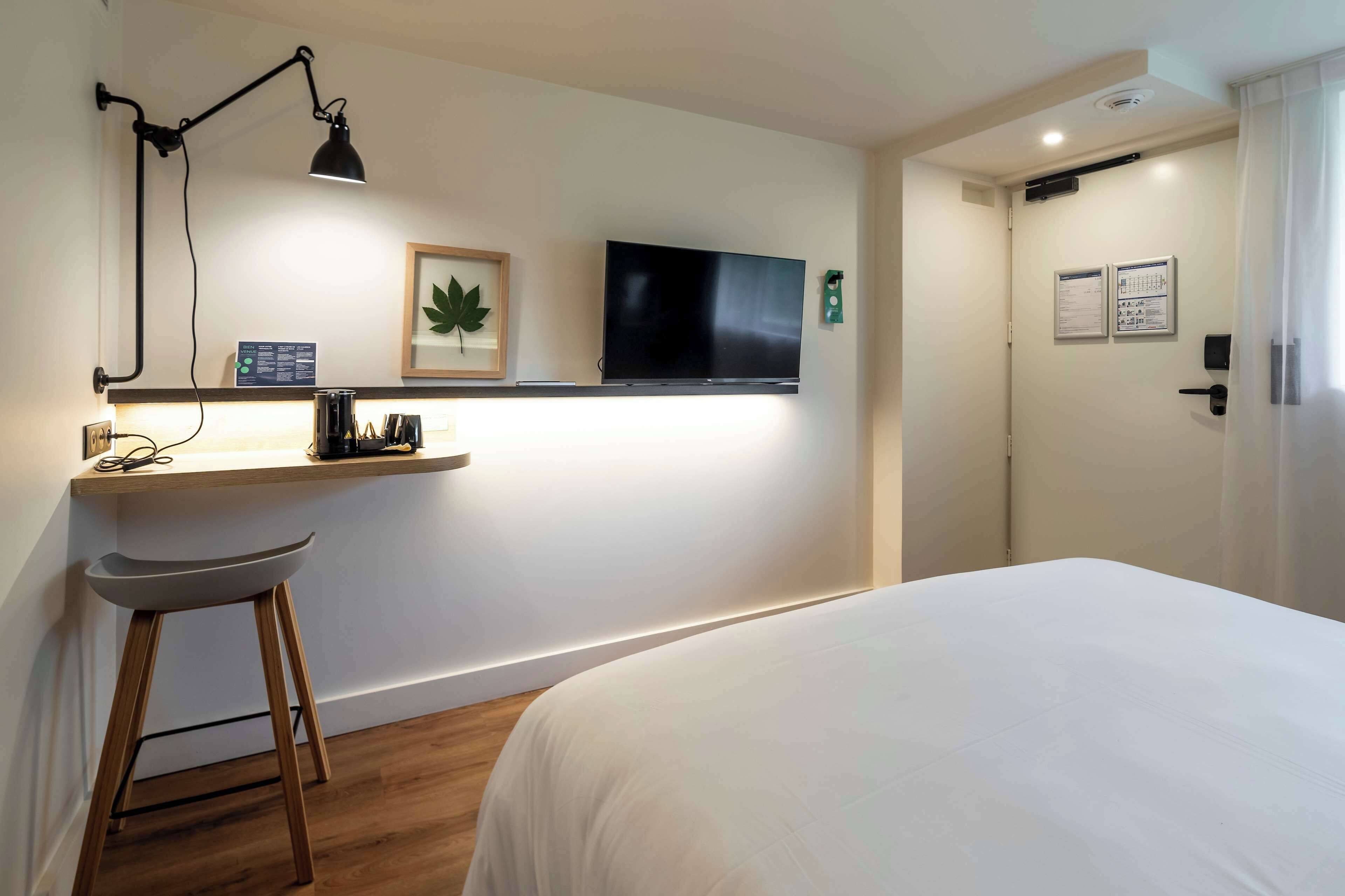 Une chambre d’hôtel comprenant un lit, un bureau avec une chaise, un téléviseur fixé au mur, une porte dotée d’une serrure et d’un lecteur de carte magnétique.