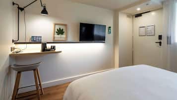 Une chambre d’hôtel comprenant un lit, un bureau avec une chaise, un téléviseur fixé au mur, une porte dotée d’une serrure et d’un lecteur de carte magnétique.