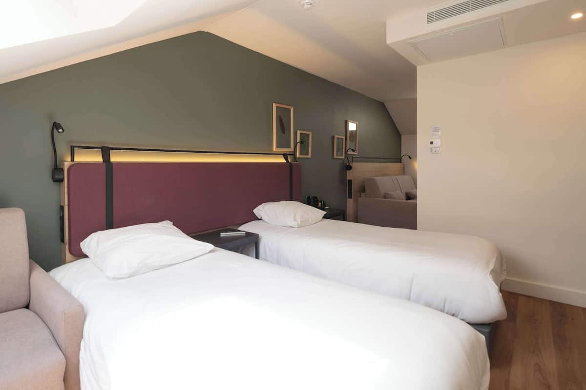 A hotel room with two single beds, a nightstand, a chair, and a small table.