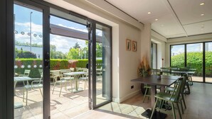 A modern indoor dining area with glass doors leading to an outdoor patio. - Campanile NATURE - Metz Sud Jouy aux Arches (Jouy-aux-Arches)