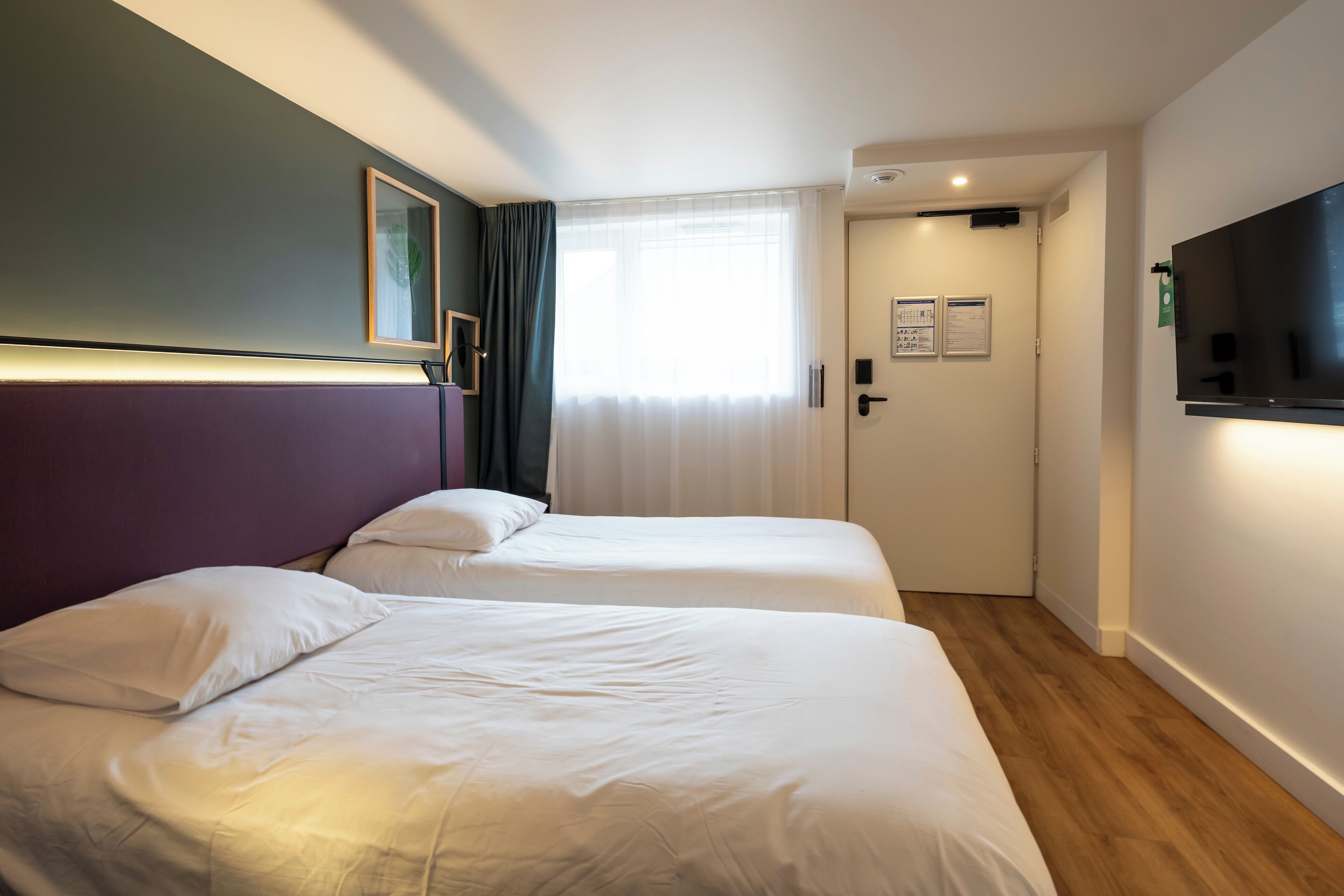 A hotel room with two beds, a TV, and a door leading to a bathroom.