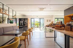 Un café moderno con zonas de estar, un mostrador con productos de panadería y vistas al exterior.
