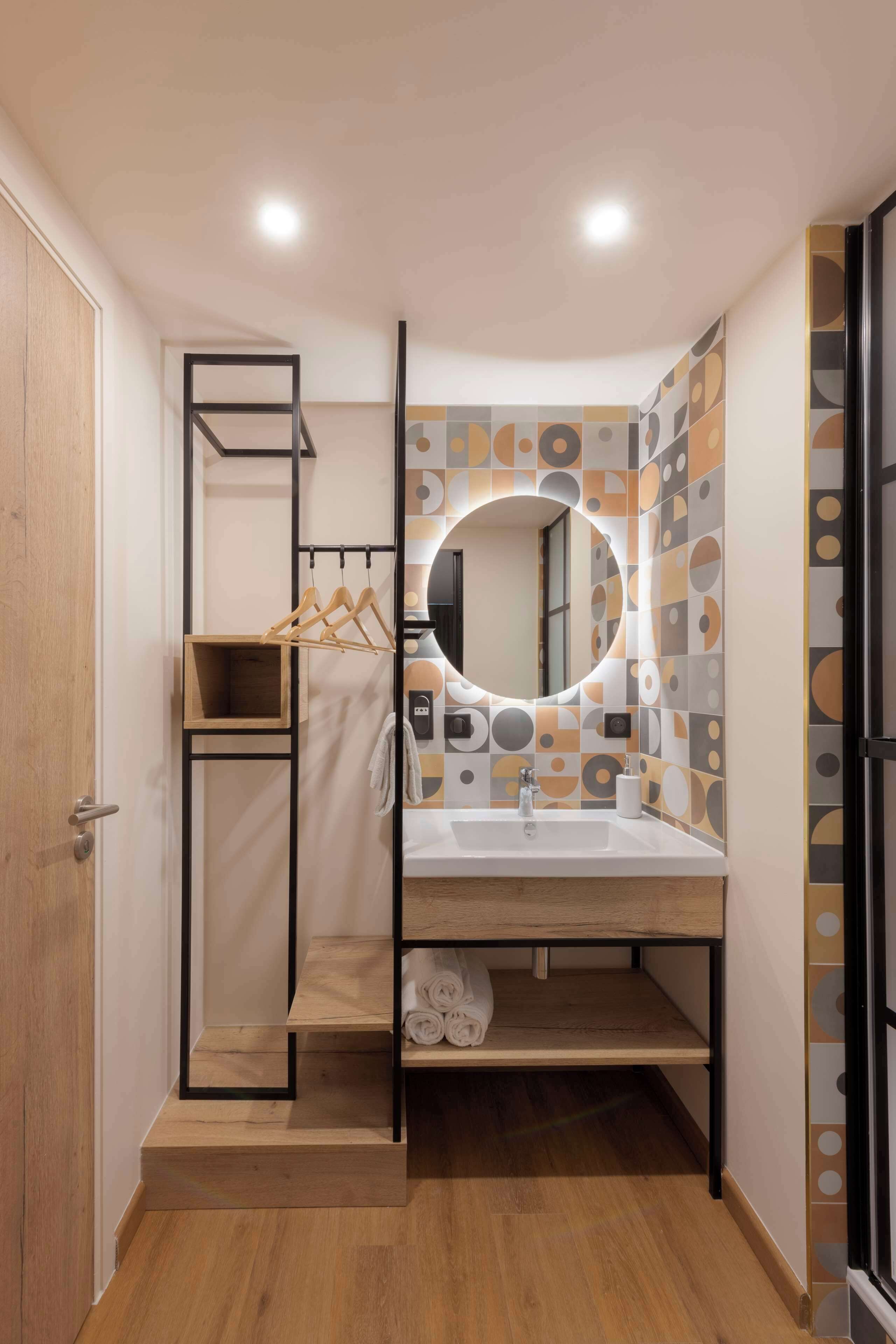 Un baño con suelo de madera, un lavabo blanco, un espejo con marco circular y un perchero para toallas.