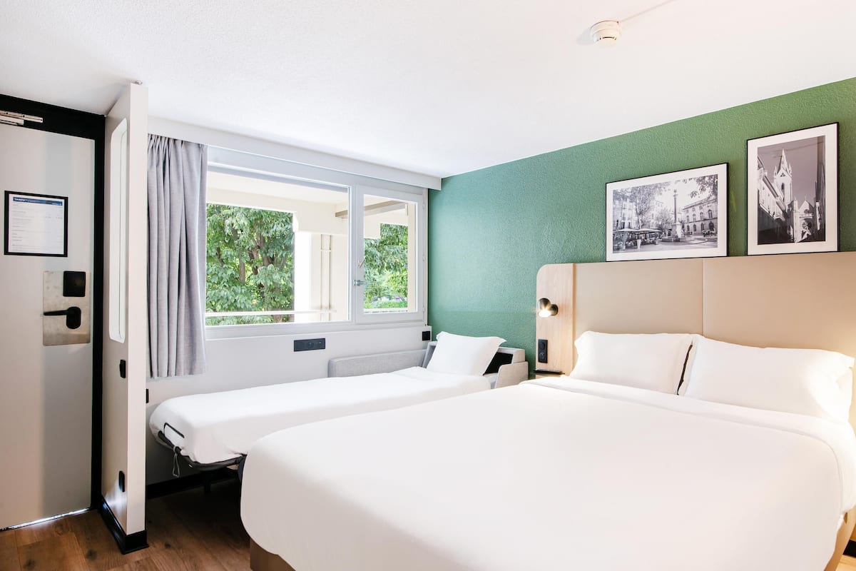 Ein Hotelzimmer mit zwei Betten, einem Fenster mit Vorhängen, einer grünen Wand und zwei gerahmten Bildern.