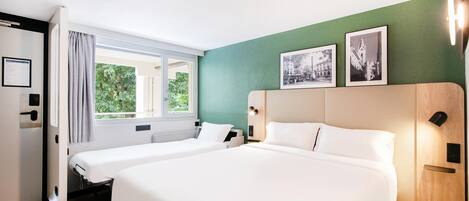 Habitación de hotel con dos camas, una ventana con cortinas, una pared verde y dos cuadros enmarcados.