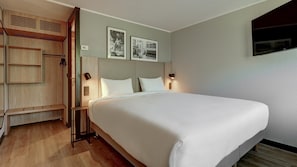 Een hotelkamer met een bed, een houten garderobe en twee ingelijste foto's aan de muur.
